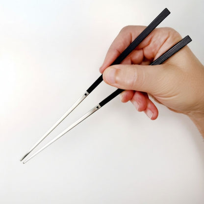 Hand holding a pair of 316 stainless steel  chopsticks with black handles against a white background
