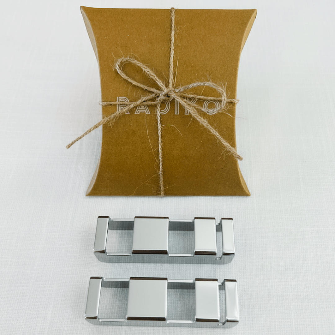 A folded kraft-paper pillow box embossed with the "RADIKO" logo and tied with twine, displayed above two sets of polished silver stainless steel chopstick rests on a white linen background.