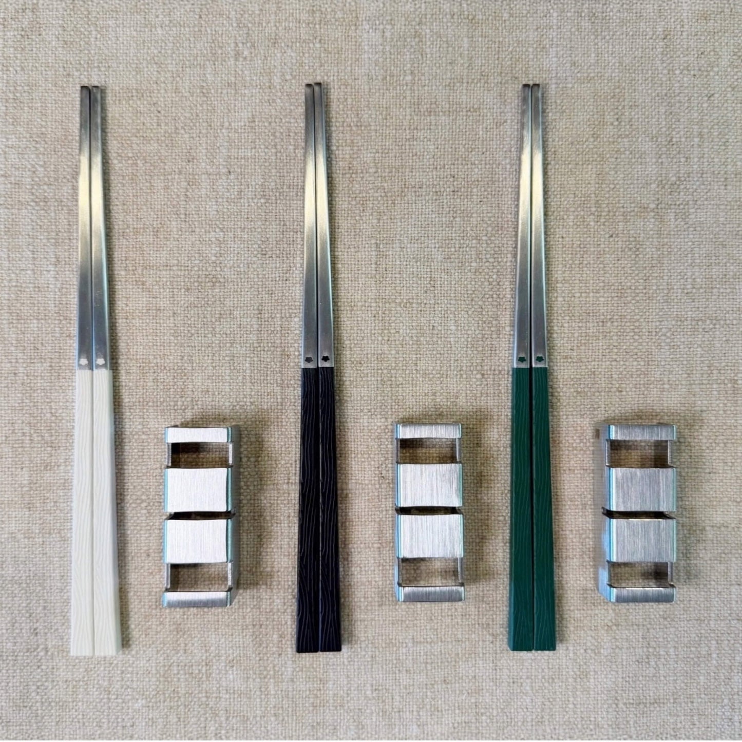 Radiko stainless steel chopsticks in white, black, and green paired with brushed steel flatware rests, arranged on natural linen